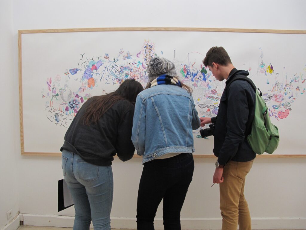 3 visiteurs sont debout devant une oeuvre