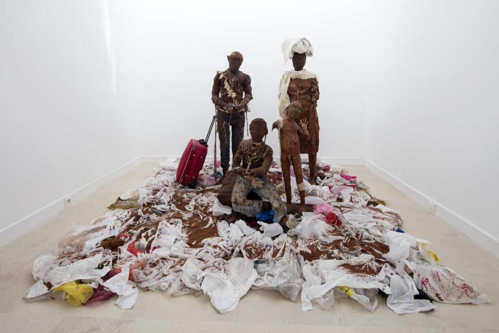 personnages réalisés en terre représentant des hommes, femme et enfants sur sol fait de sacs plastiques