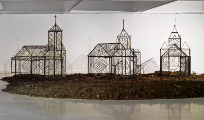 un tas de terre recouvre le sol de la galerie devant 3 maquettes d'églises réalisées en fer forgé