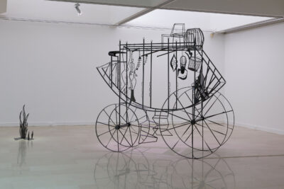 Sculpture en métal noir représentant une cariole dans un espace blanc.