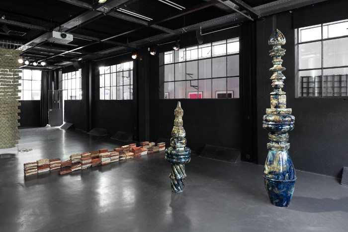 Deux sculptures en céramique dans une salle sombre, éclairée par de larges baies
