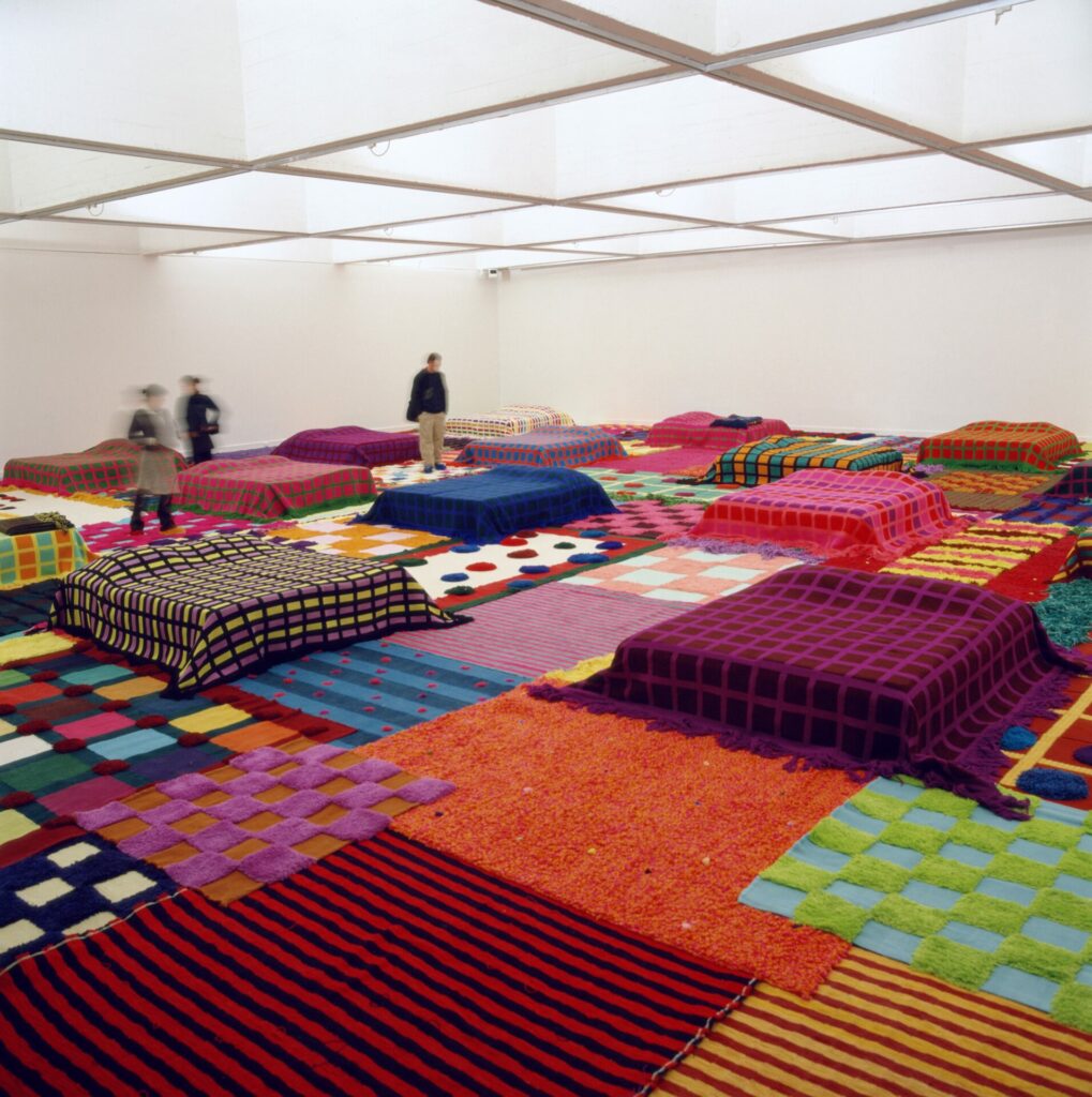 installation avec lits de camps, tapis, couvertures, textiles divers